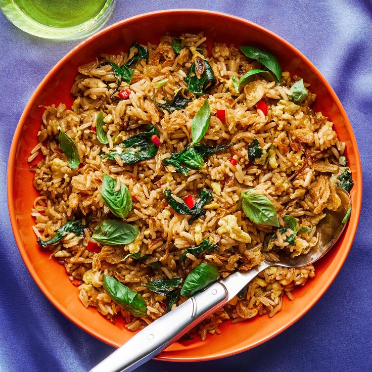 an orange bowl filled with rice and spinach next to a glass of green tea