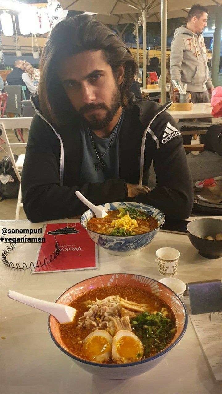 a man with long hair sitting at a table in front of a bowl of food