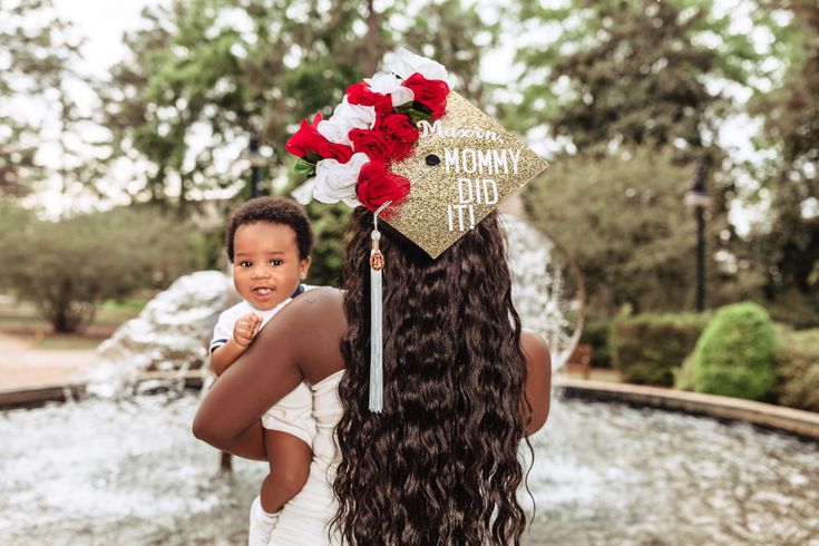 a woman holding a child in her arms and wearing a graduation cap with flowers on it