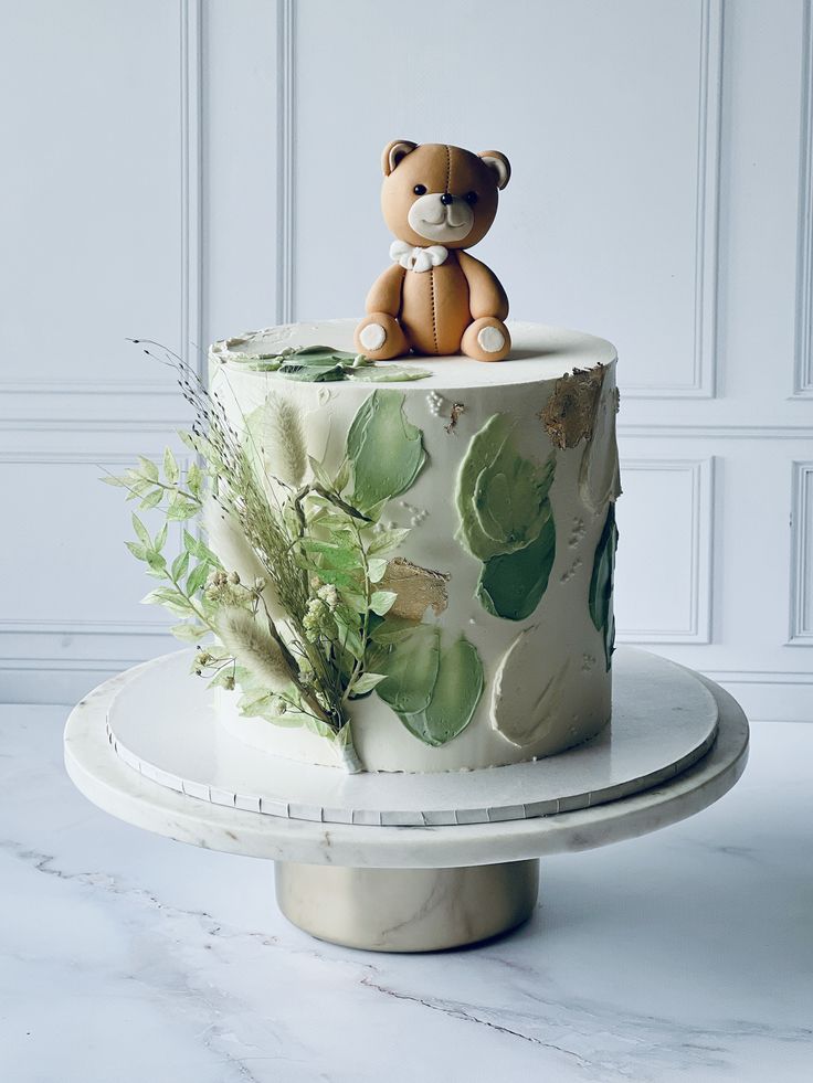 there is a cake decorated with leaves and a teddy bear sitting on top of it