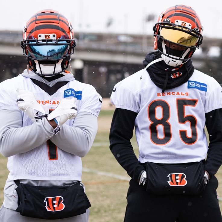 two football players standing on the field with their arms crossed and helmets folded over their shoulders