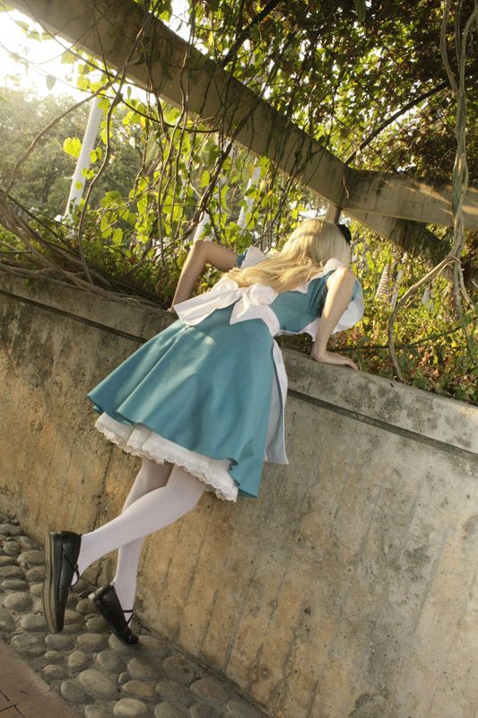 a woman is leaning against a wall with her legs on the ground, wearing a blue dress and white tights