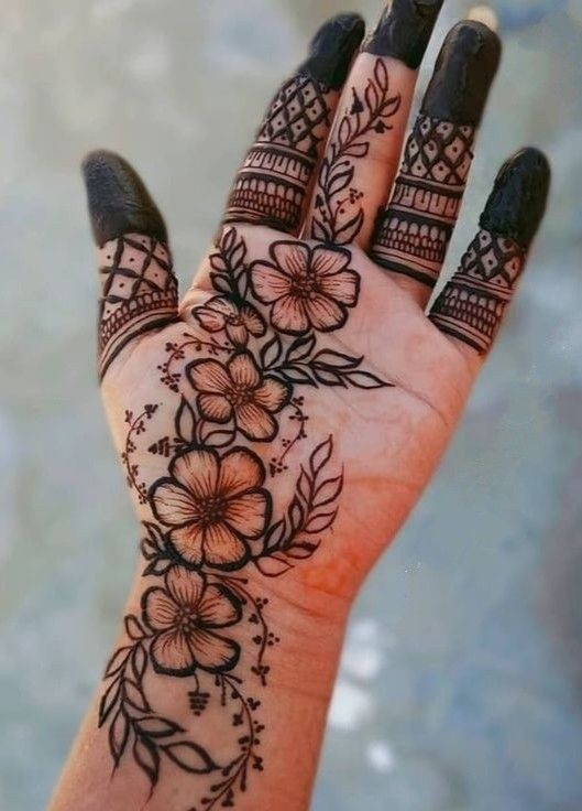 a woman's hand with henna tattoos and flowers on the palm, which is decorated