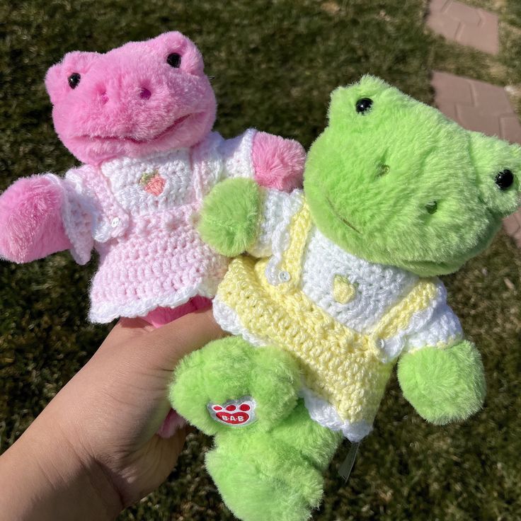 two stuffed animals in crocheted clothes are being held by someone's hand