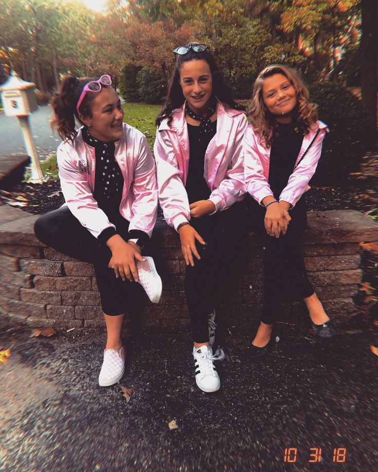 three women sitting on a brick wall in pink jackets and black pants with white sneakers