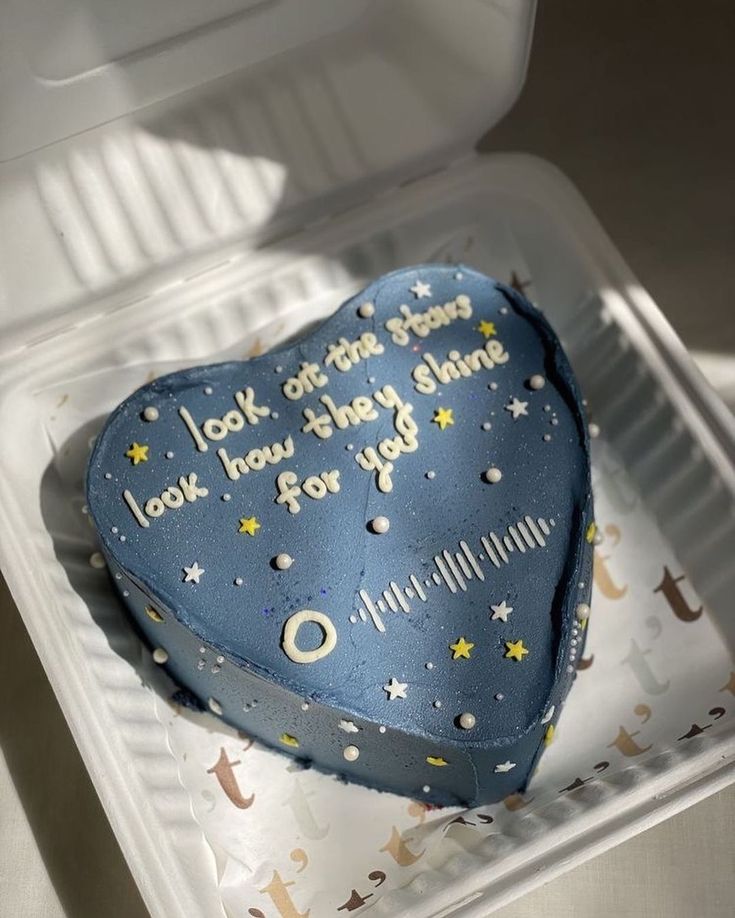 a blue heart shaped cake with writing on it sitting in a plastic container that says look at the stars i love how they stay there for you