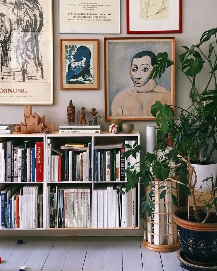 a bookshelf filled with lots of books next to potted plants and pictures on the wall