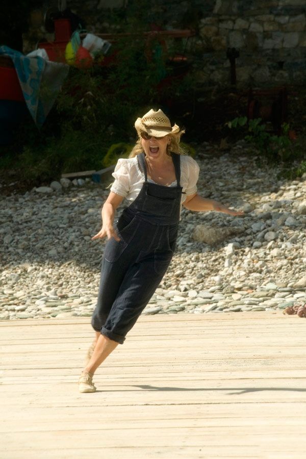 a woman wearing overalls and a straw hat is throwing a frisbee