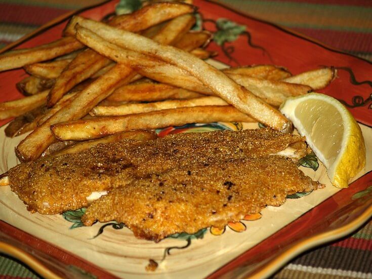 fish and french fries on a plate with lemon wedges next to it, sitting on a tablecloth