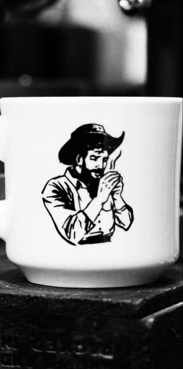 a black and white photo of a coffee cup with a drawing of a man wearing a cowboy hat