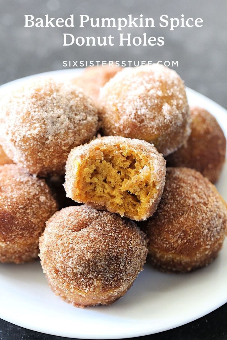 a white plate topped with sugar covered doughnuts on top of a black table