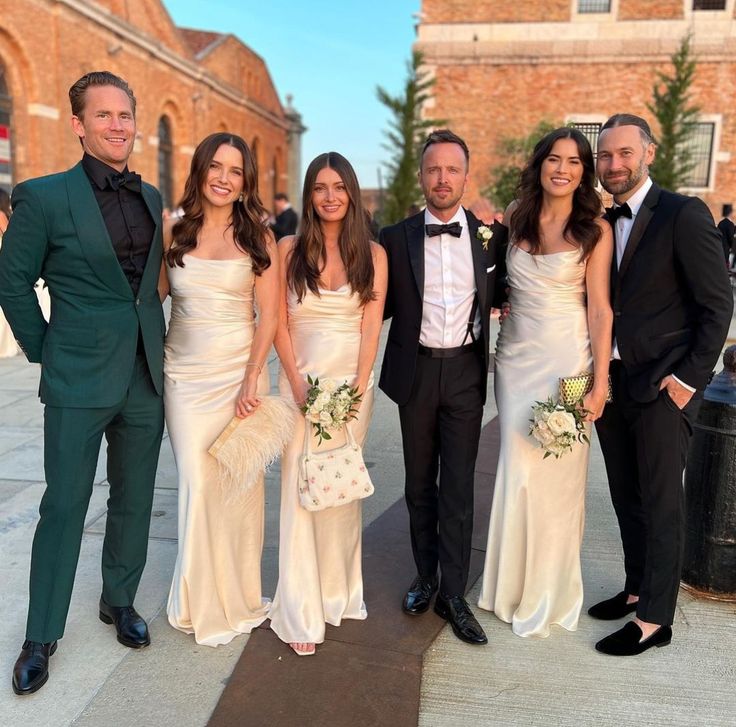 a group of people standing next to each other in formal wear and tuxedos