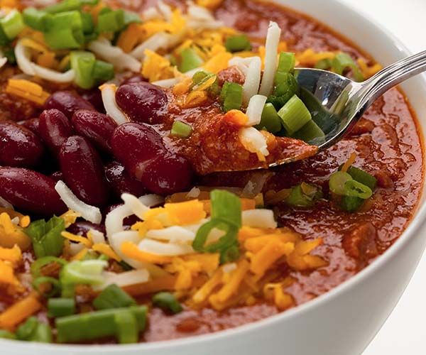 a white bowl filled with chili and beans topped with green onions, cheese and jalapenos