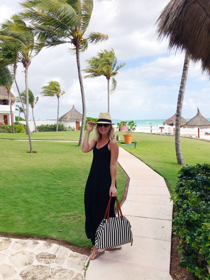 a woman in a black dress and hat is carrying a striped bag on the sidewalk