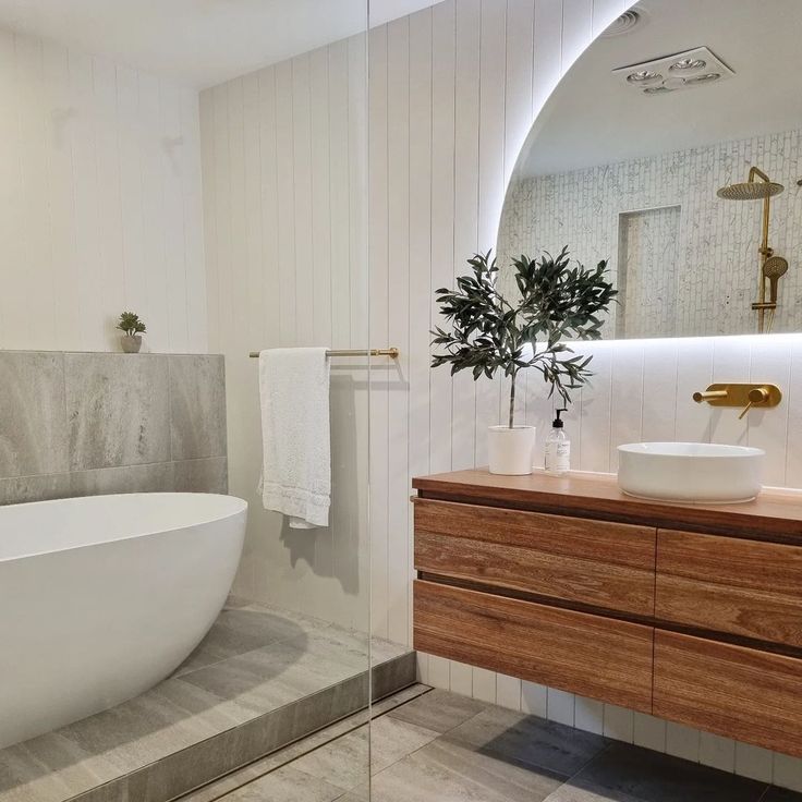 a white bath tub sitting next to a wooden counter top under a bathroom mirror above a sink