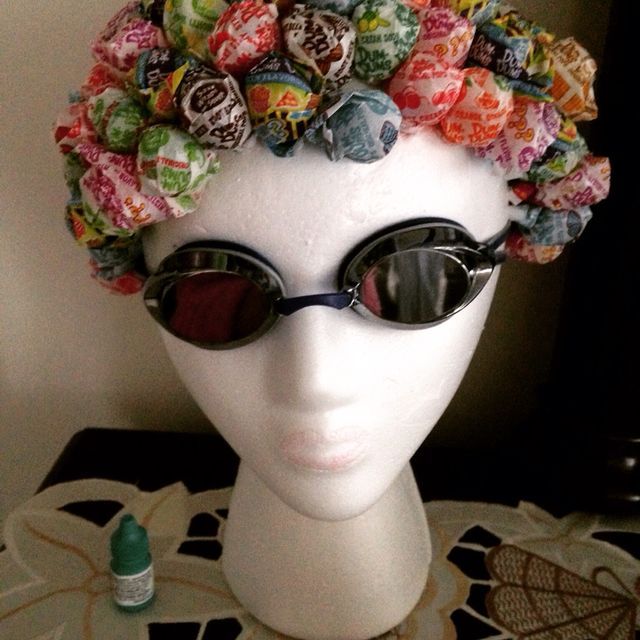 a white mannequin head wearing sunglasses and a hat with candy buttons on it