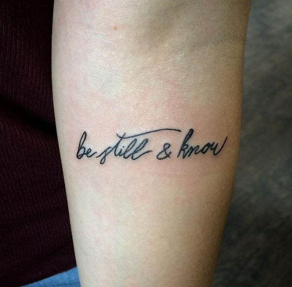 a woman with a tattoo on her arm that says, be still and know in cursive writing