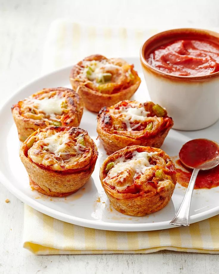 several mini pizzas on a white plate with sauce in a bowl next to them