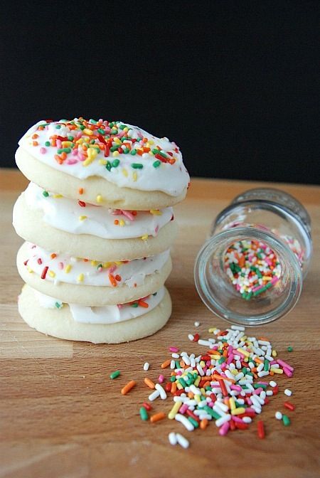 a stack of cookies with sprinkles next to a glass jar on a wooden table