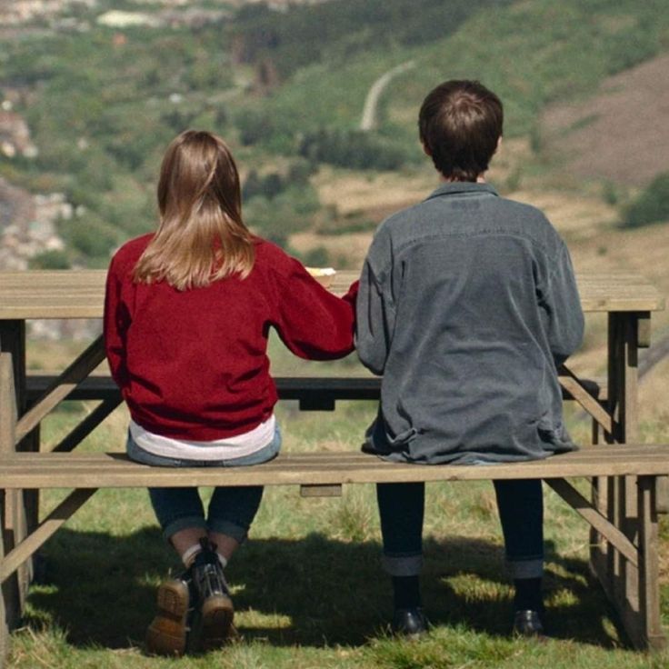 two people sitting on a bench looking out over the valley and town in the distance