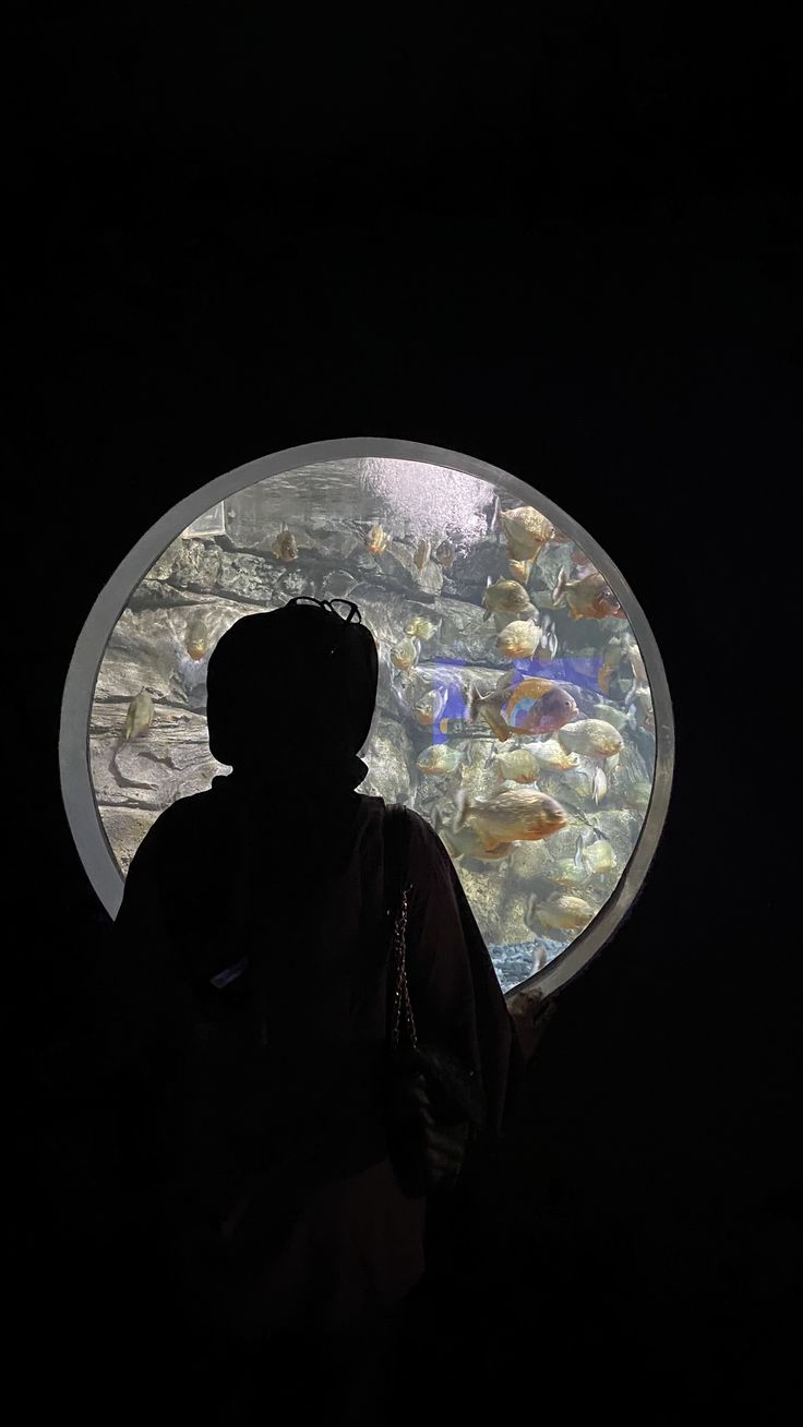 a man standing in front of an aquarium looking into the light at it's reflection