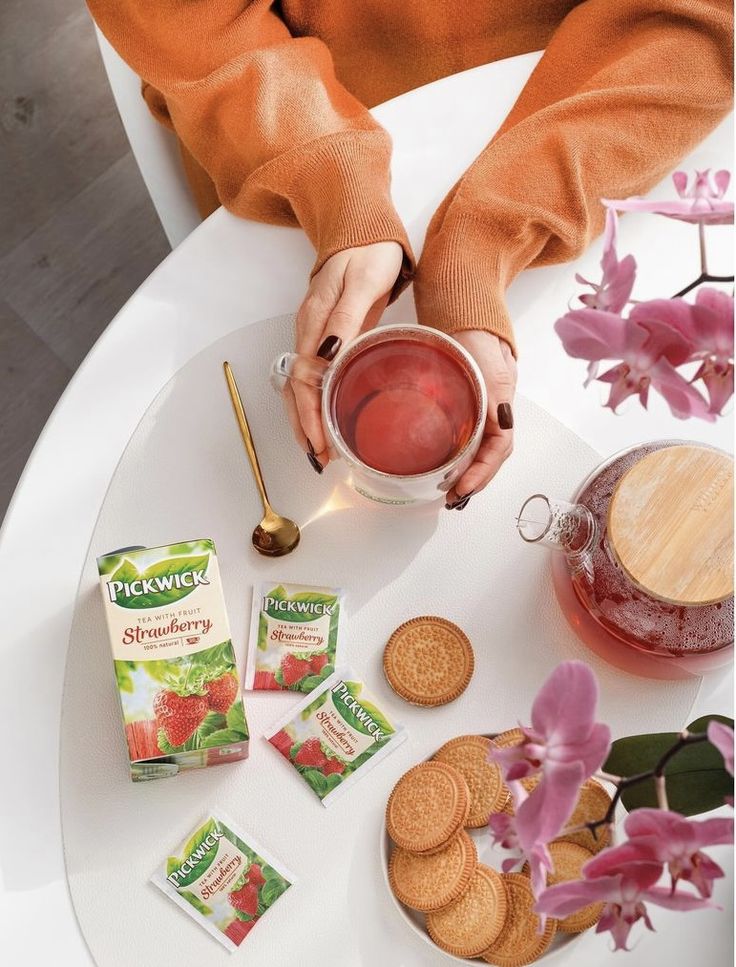 a woman is holding a cup with tea and cookies on the table next to her