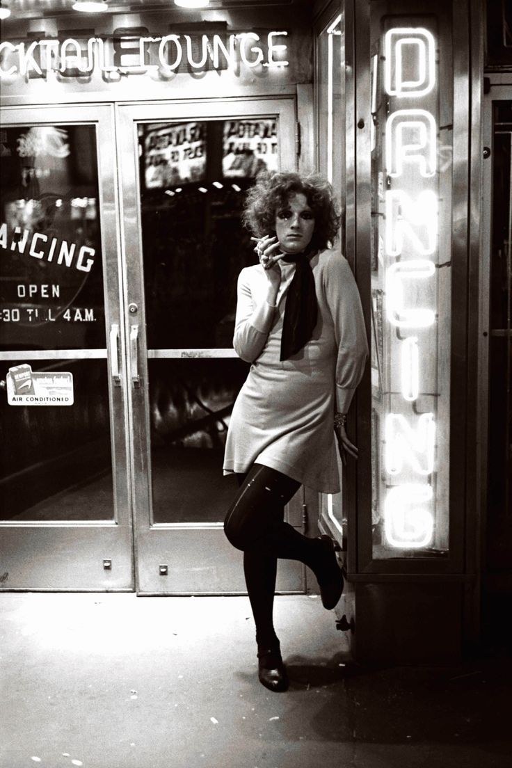 a woman is standing on the sidewalk talking on her cell phone in front of a neon sign