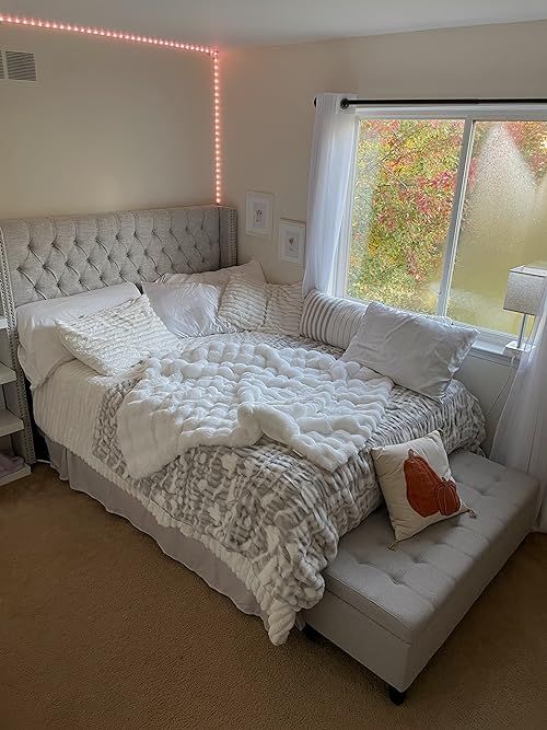 a white bed sitting next to a window in a bedroom under a light that is on