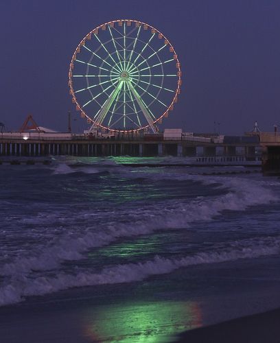 a ferris wheel sitting on top of a pier next to the ocean under a purple sky