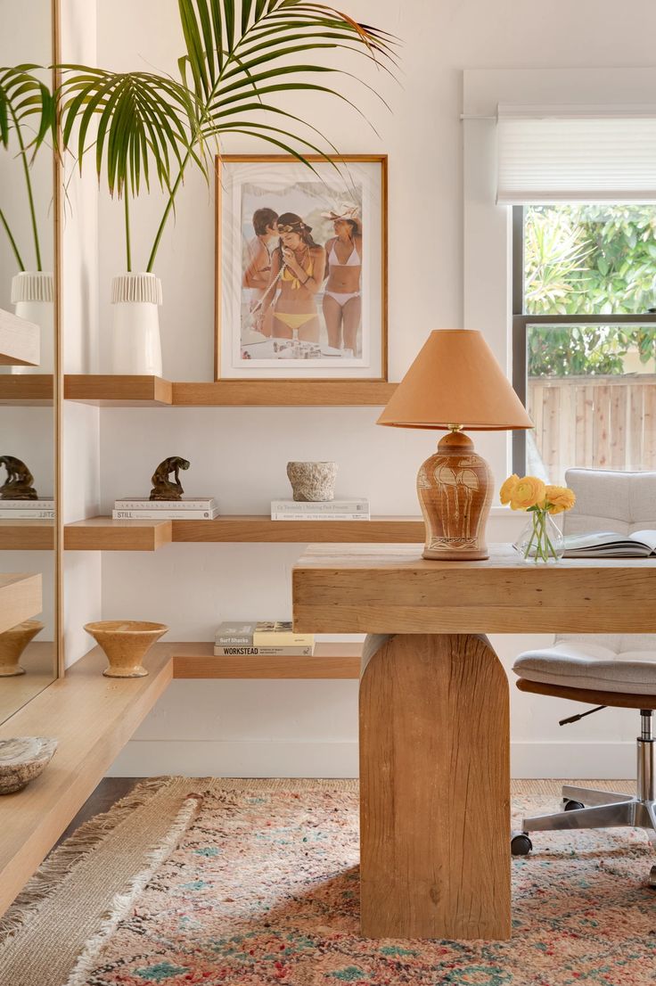 a desk with a lamp, vase and pictures on the wall above it in a living room