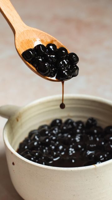 a spoon full of black olives is being lifted from a white bowl with dark chocolate sauce