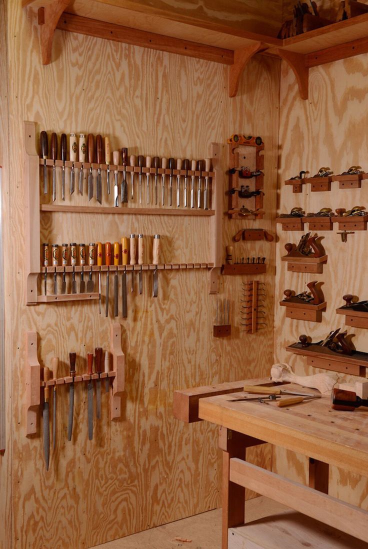 a workbench with lots of tools on the wall and wooden shelves above it