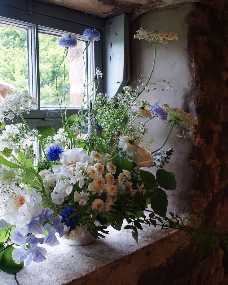 a vase filled with white and blue flowers sitting on top of a window sill