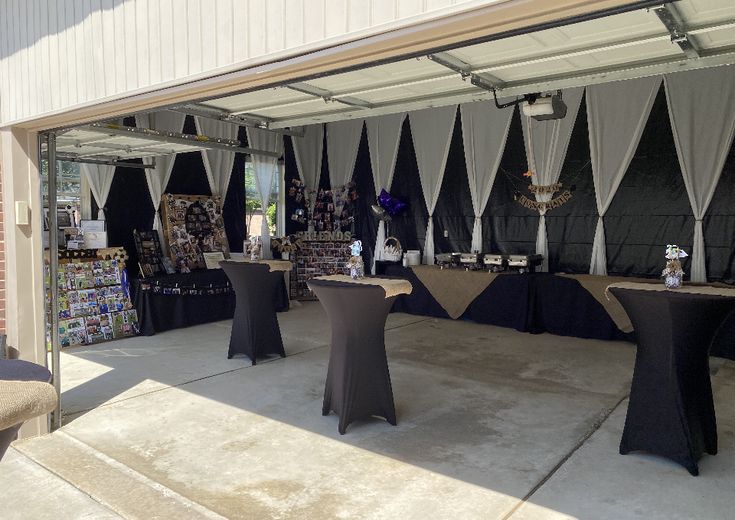 an outdoor event with tables covered in black tablecloths and white draping