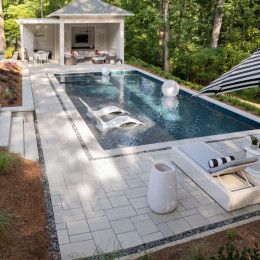 an outdoor swimming pool with lounge chairs and umbrellas next to it, surrounded by trees