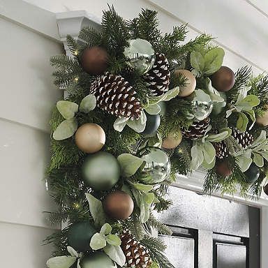 a christmas wreath with pine cones and greenery hanging from the front of a house