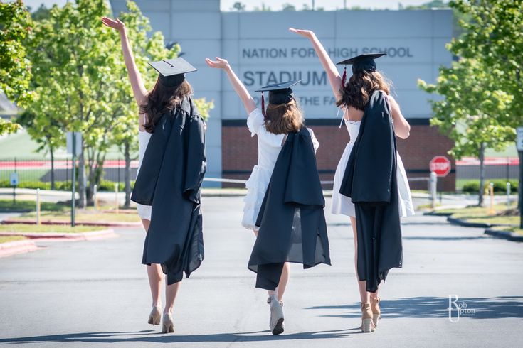 three women in graduation gowns and caps are walking down the street with their arms up