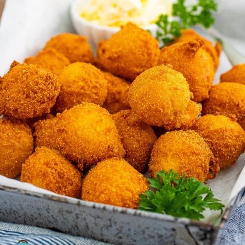 homemade hush puppies in a tin with parsley on the side