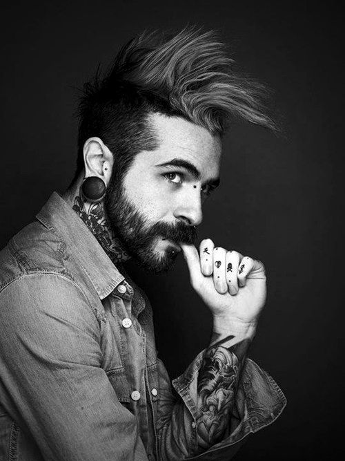 a man with tattoos and piercings on his ears is posing for a black and white photo