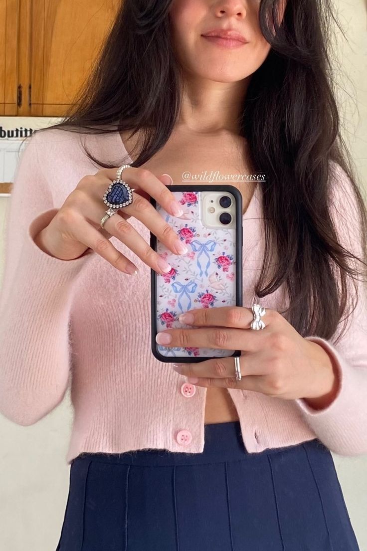 a woman in a pink sweater is holding her cell phone up to the camera while wearing a ring