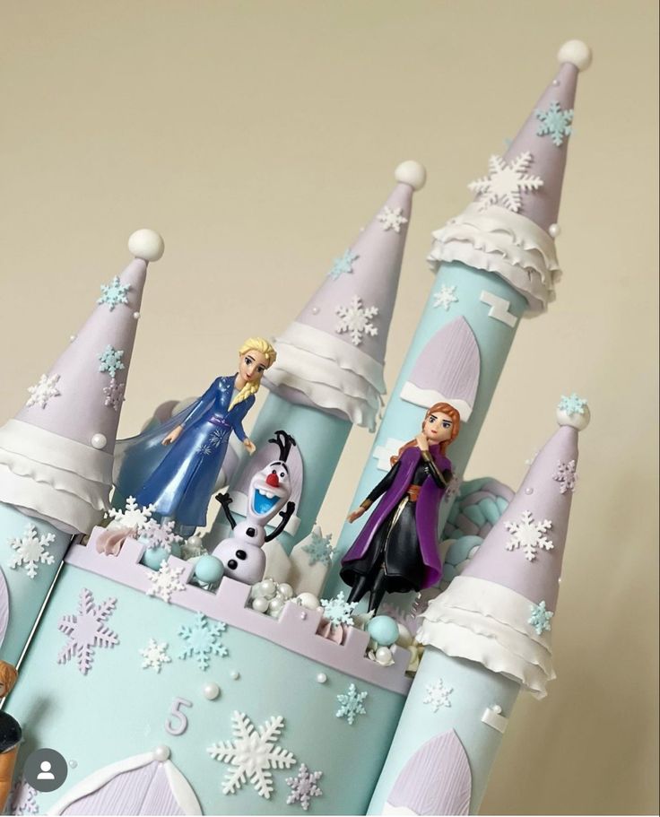 there is a cake that looks like a castle with frozen princess figures on it and snowflakes all around