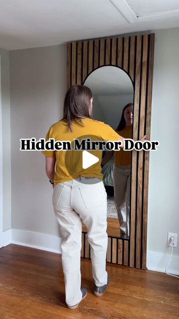 a woman standing in front of a mirror with her reflection on the wall behind her