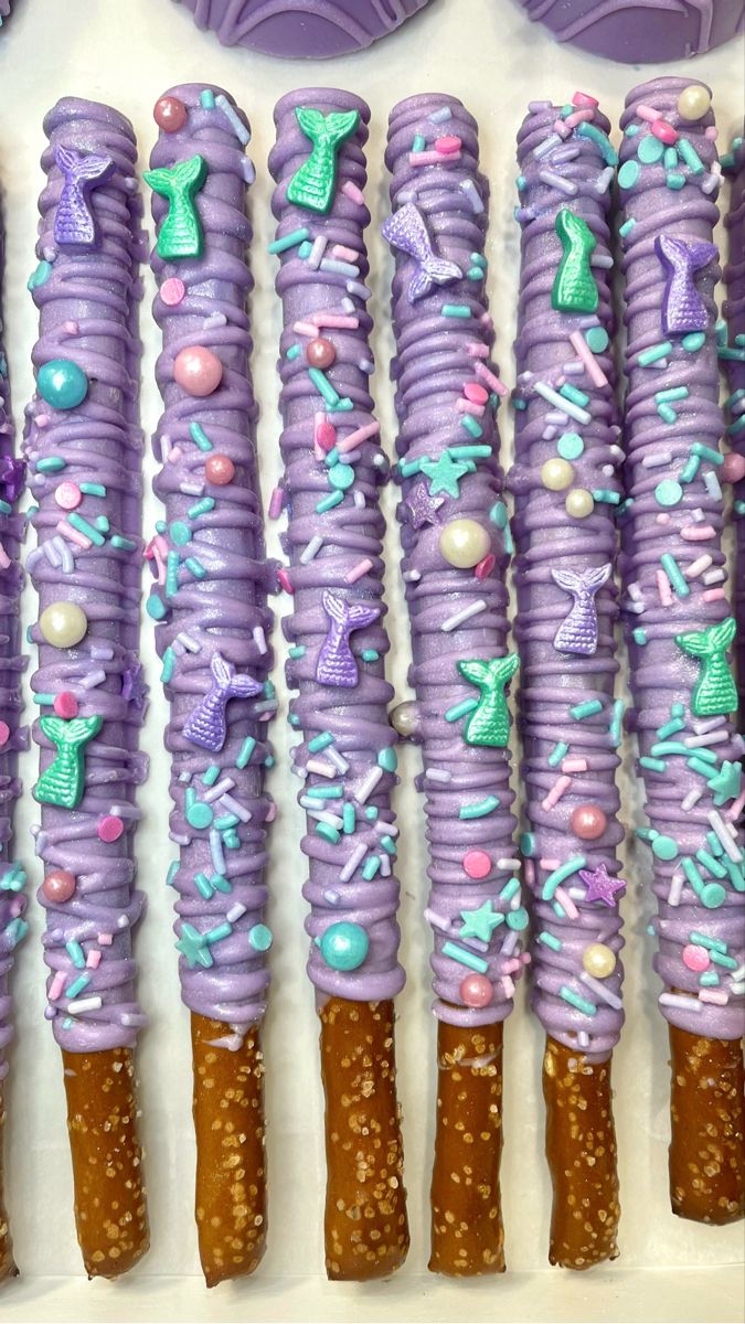 purple and blue decorated desserts are lined up on a white surface next to cookies