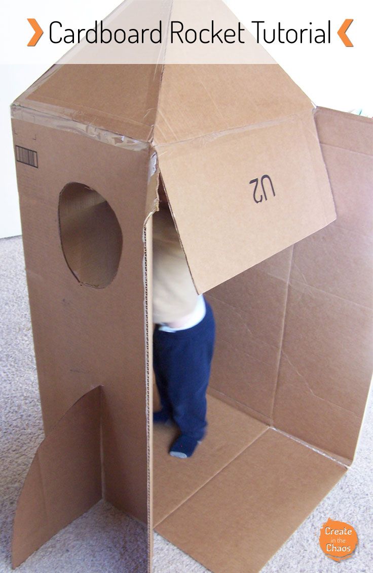 a cardboard rocket ship with the door open and a child standing in front of it