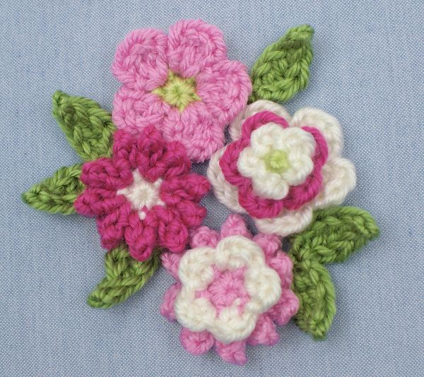 crocheted flowers with green leaves on a blue background, ready to be made into brooch pins