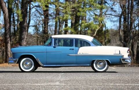 an old blue and white car parked on the side of the road in front of some trees