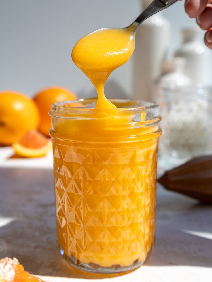 a person is spooning orange juice into a jar