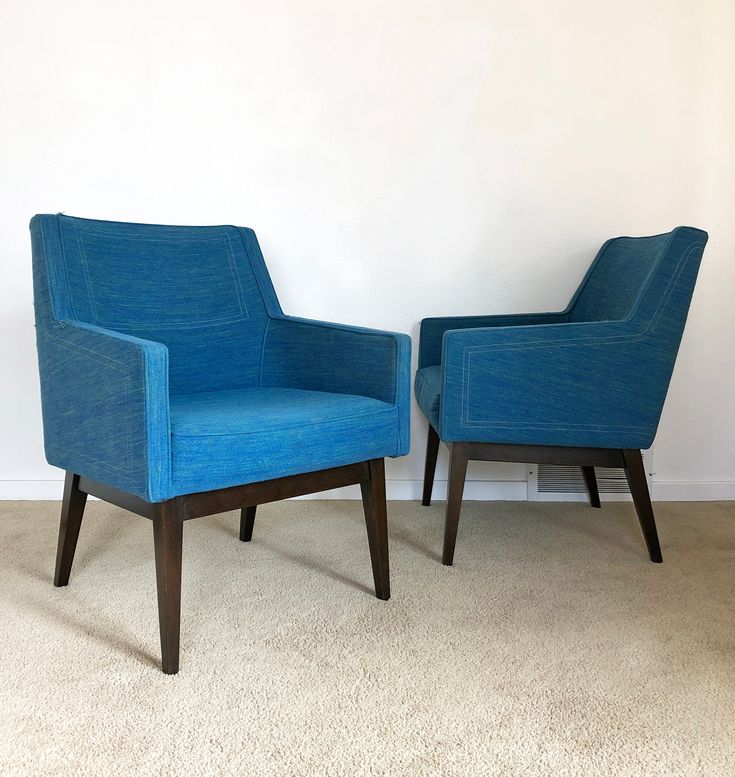 two blue chairs sitting next to each other on top of a carpeted floor in front of a white wall