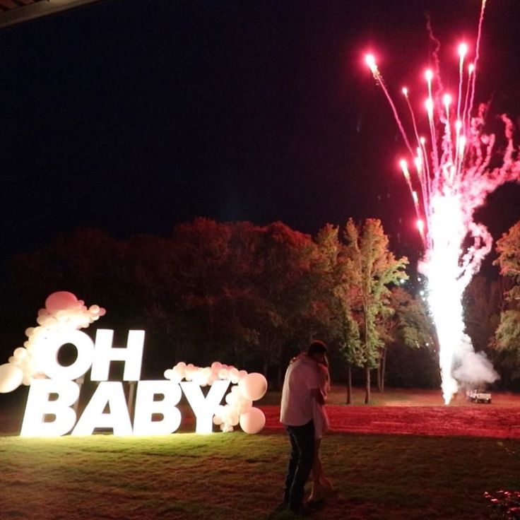 two people standing in front of a sign that says oh baby with fireworks behind it