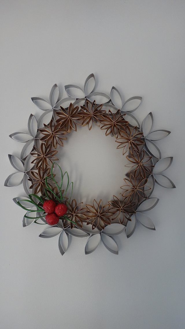 a metal wreath with red berries and green leaves on the front, hanging on a white wall